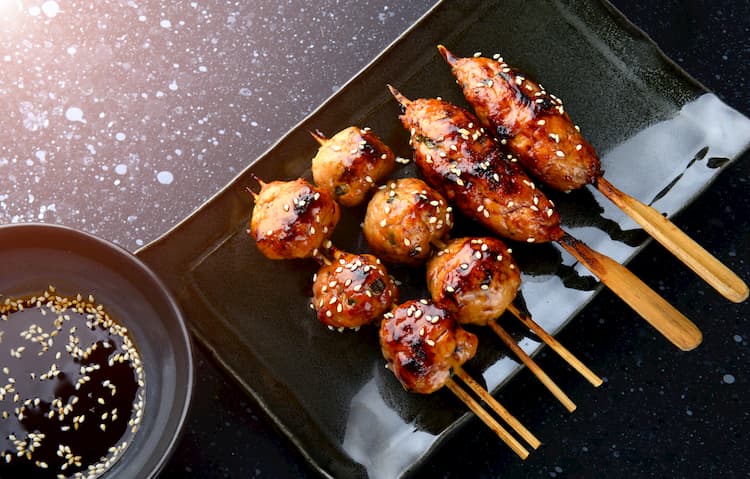 grilled meat on wood skewers arranged on a dark plate