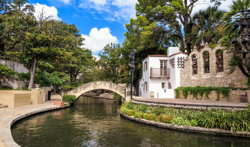 View of an old adobe-style building and stone bridge crossing the San Antonio River in La Villita in San Antonio