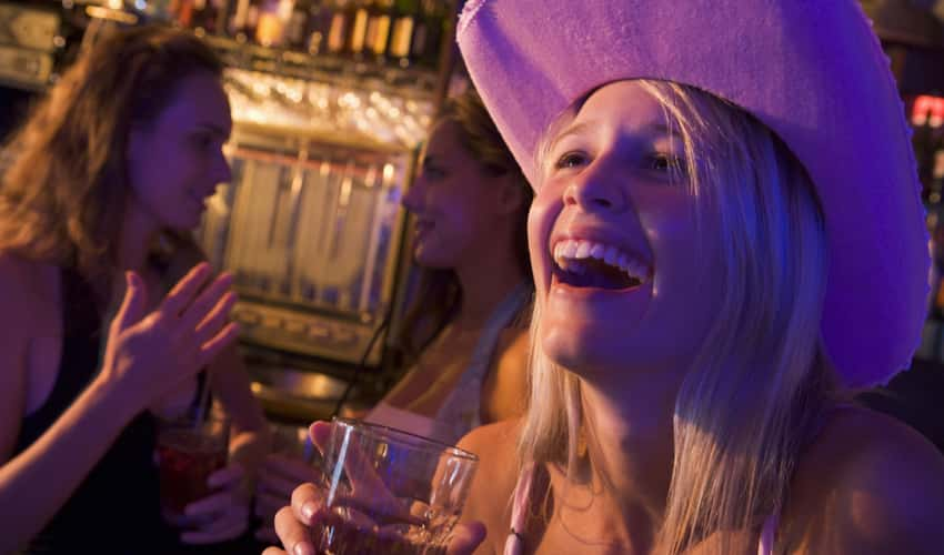 A woman in a cowboy hat smiling and drinking with friends at a bar