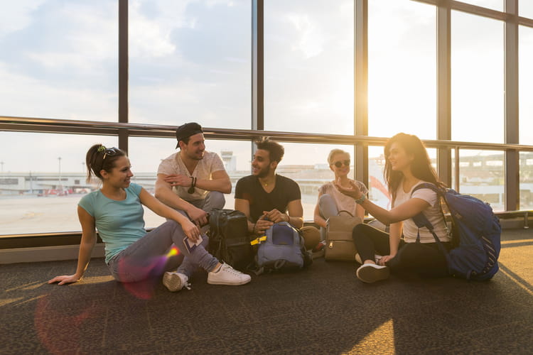 friends sit on the floor near a large window and wait for their flight