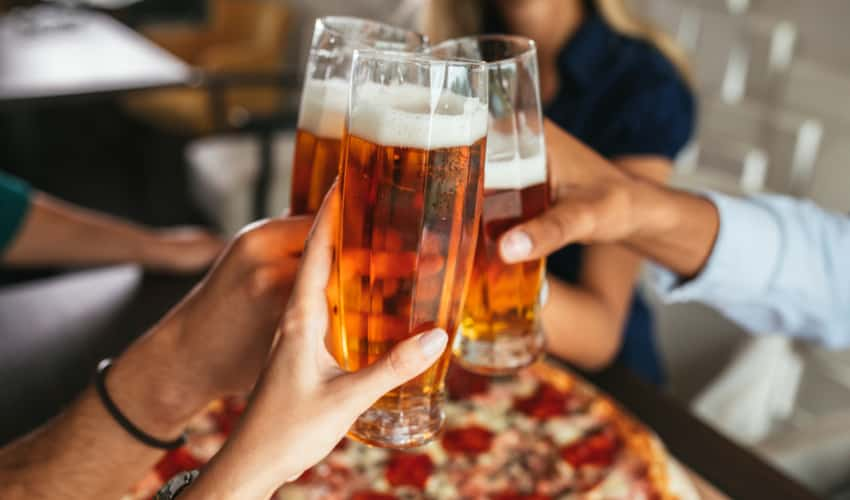 People toasting beer over a pizza