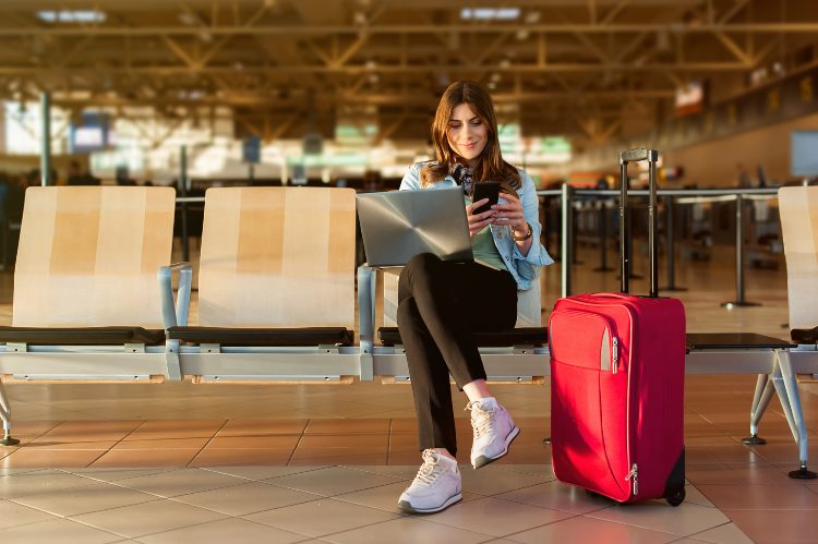 a woman sits with her laptop and checks her phone in an airport lobby