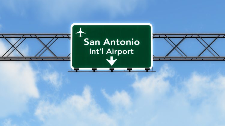 a sign against a cloudy blue sky that reads "san antonio int'l airport"