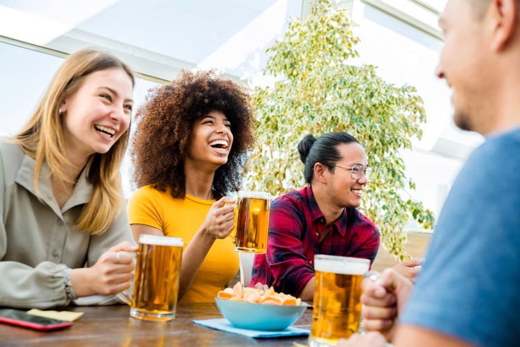 friends laugh as they sit around a table at a brewery