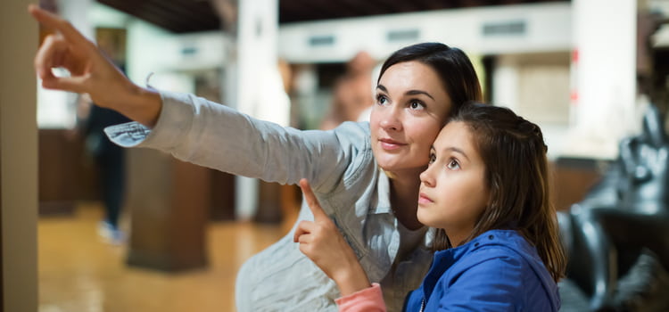 a mother and her daughter point at a piece of work in a museum